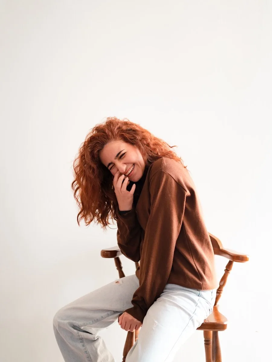 Woman with curly red hair laughing on a chair